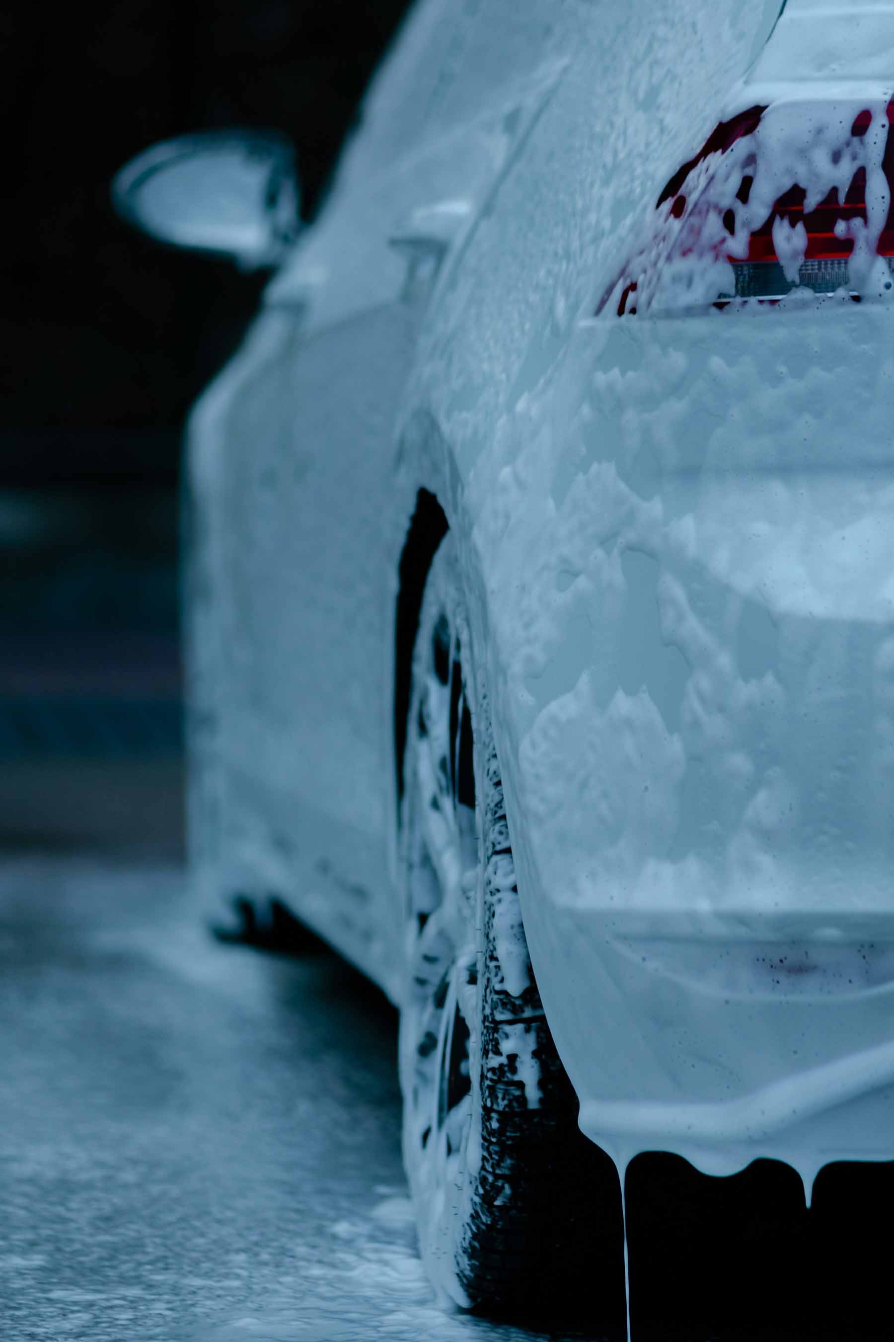 oiture en cours de lavage avec mousse de nettoyage coulant sur la carrosserie, mettant en avant un service de detailing automobile à Genève par Alfredo Services.